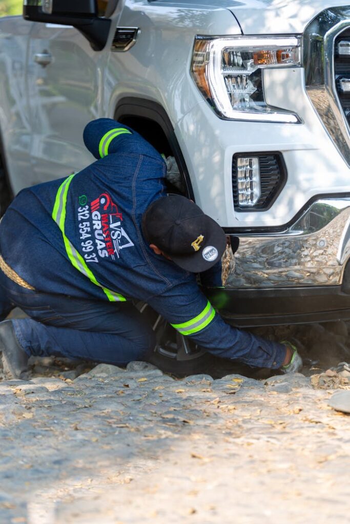 Mechanic works on a white truck on a rocky roadside, emphasizing repair and service.