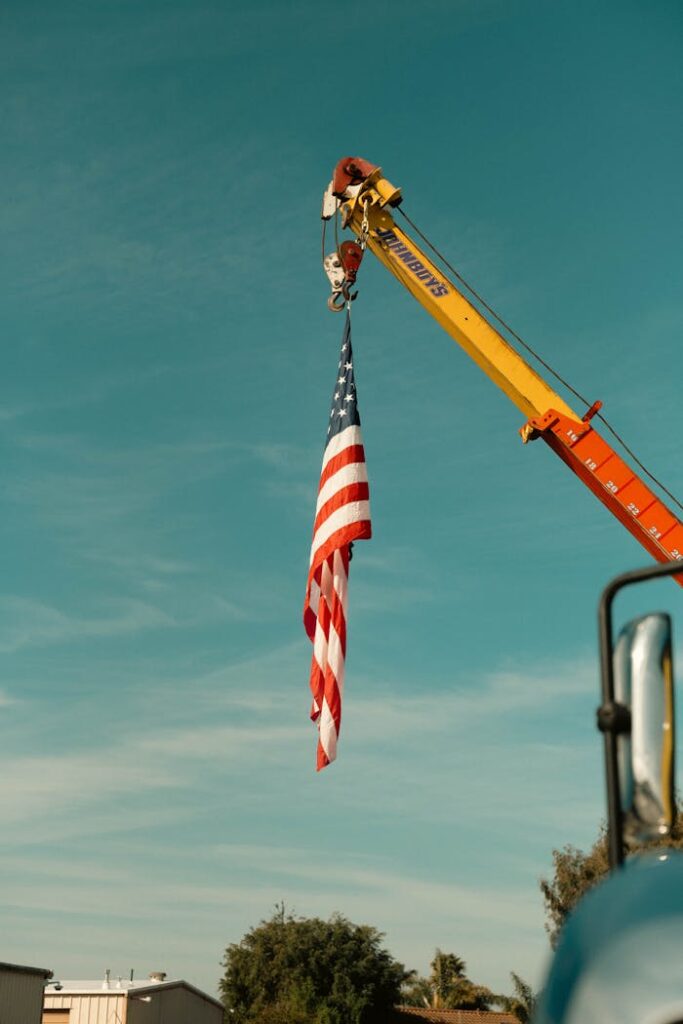 A construction crane hoists an American flag against a clear blue sky.